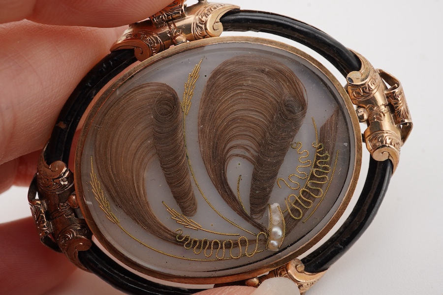 A Victorian yellow metal and black enamel oval mourning brooch, with plaited hair beneath a glazed panel, the back inscribed 'In Memory of Alex Rae died 21st Aug. 1848, A.B.', 53mm.